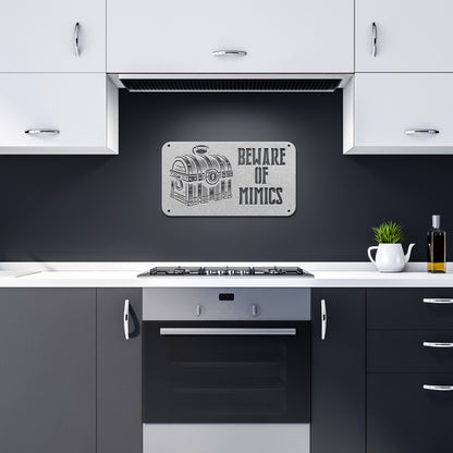 "Beware of Mimics" metal sign with a treasure chest graphic, playfully warning of hidden dangers. Ideal for TTRPG and gaming decor, made of 18-gauge steel and available in black, red, white, copper, or silver. Comes in six sizes ranging from 12 to 36 inches.